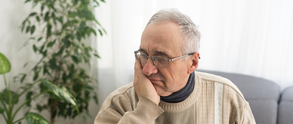 Older man sitting in chair and rubbing jaw in pain